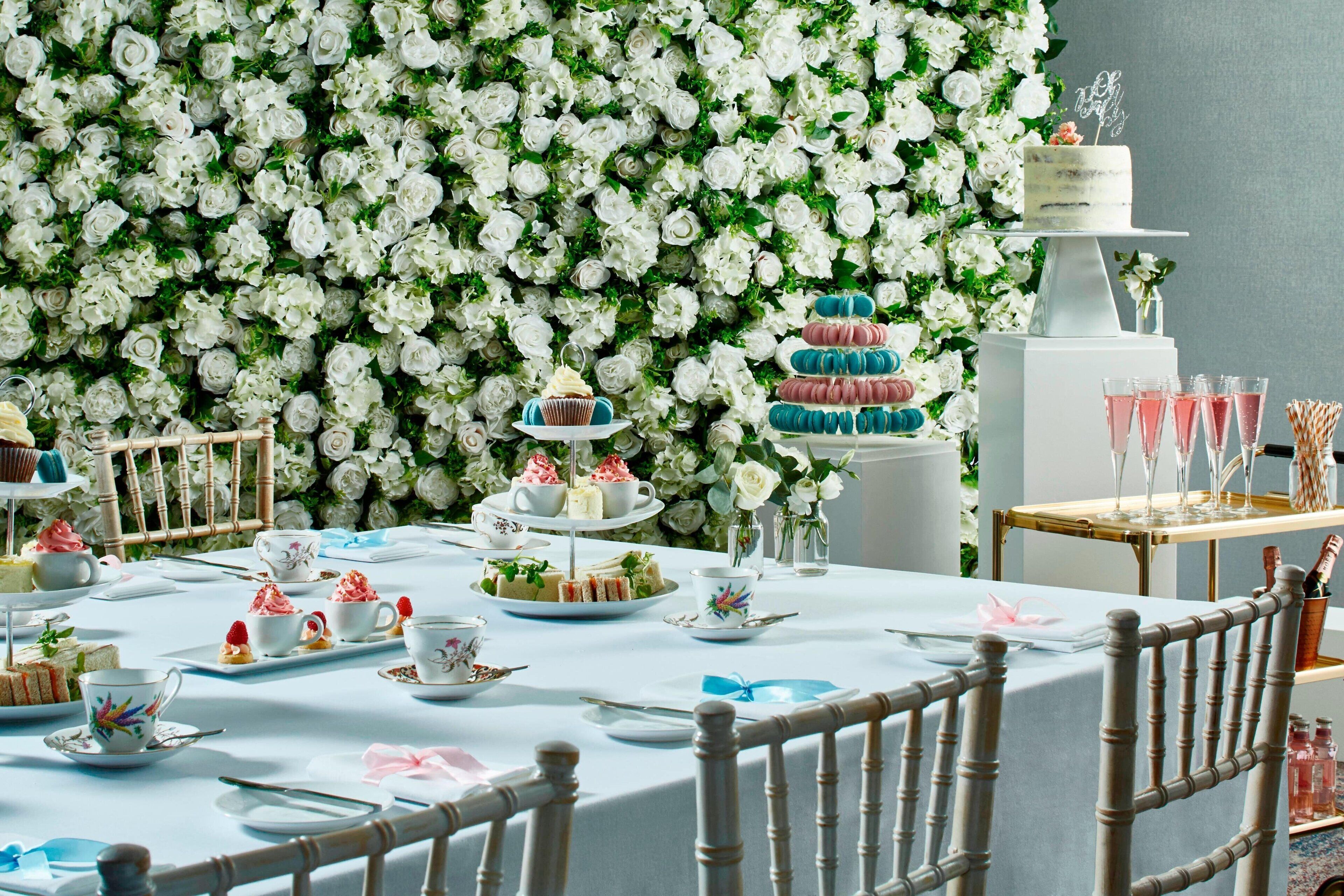 A table set for a tea party with floral decorations and a cake on a pedestal.