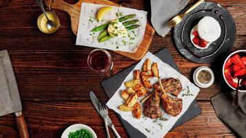 A wooden table with a variety of dishes including grilled meat, roasted potatoes, asparagus, and a dessert with strawberries.