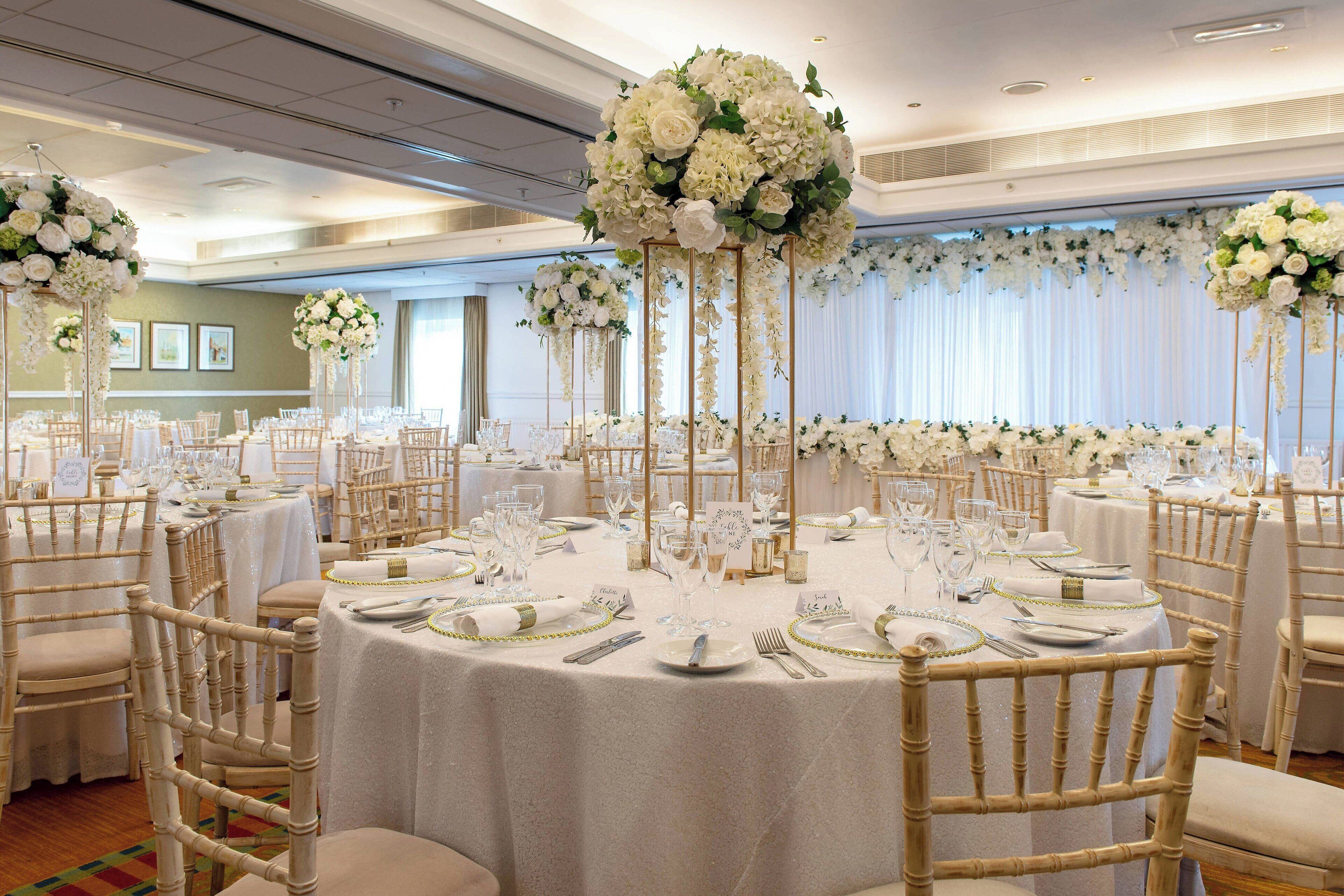 A banquet hall with round tables set for a formal event, featuring white tablecloths and floral centerpieces.