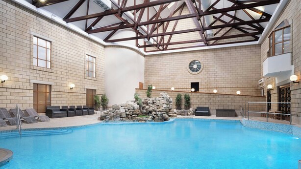 An indoor swimming pool with a stone feature, lounge chairs, and a high ceiling with wooden beams. - Delta Hotels by Marriott Tudor Park Country Club (Maidstone)