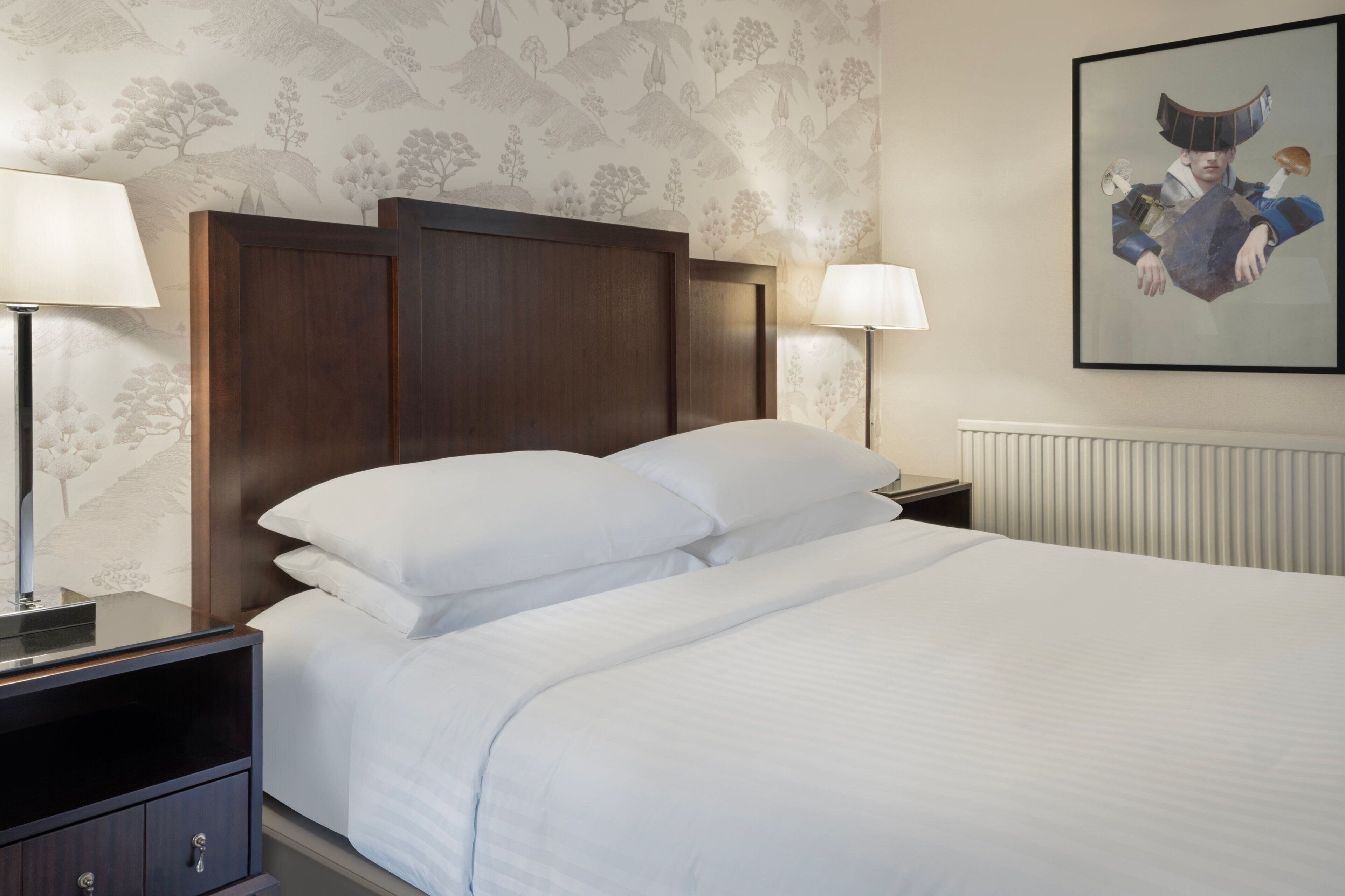 A neatly made bed with white linens, a dark wooden headboard, and a nightstand with a lamp.
