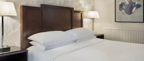 Un lit bien fait, avec du linge de lit blanc, une tête de lit en bois foncé et une table de chevet avec une lampe.