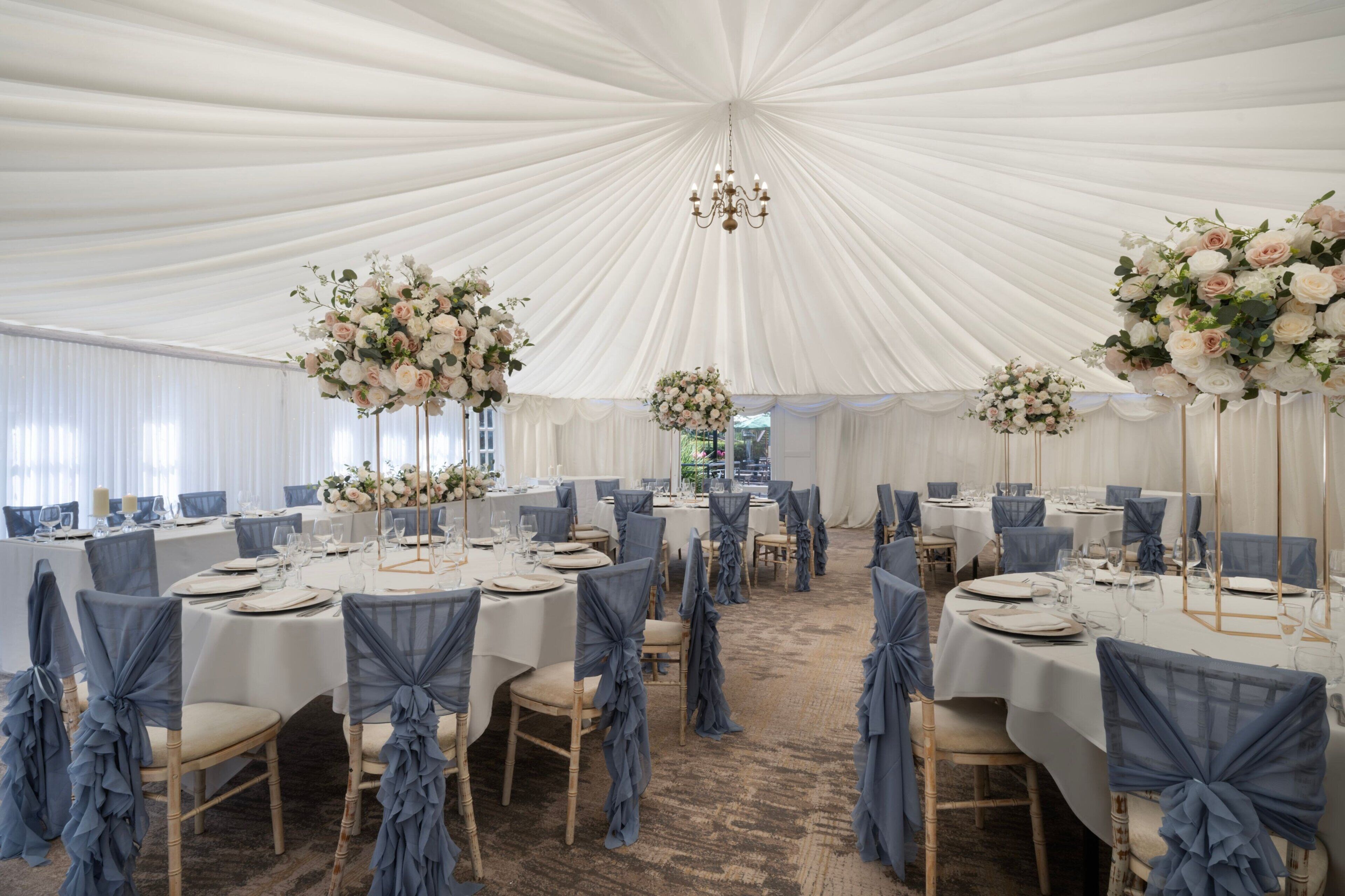 A tented event space with round tables, chairs, and floral centerpieces.
