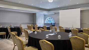 Un salón de conferencias con mesas redondas, sillas y una pantalla para proyector.