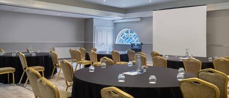 A conference room with round tables, chairs, and a projector screen.