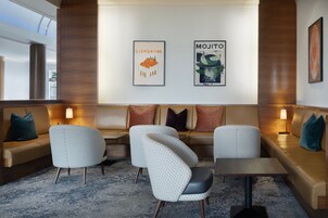 Un espacio lounge moderno con un sofá, dos sillones y una mesita. Hay dos carteles enmarcados en la pared, uno que dice "Clementine" y el otro "MOJITO".
