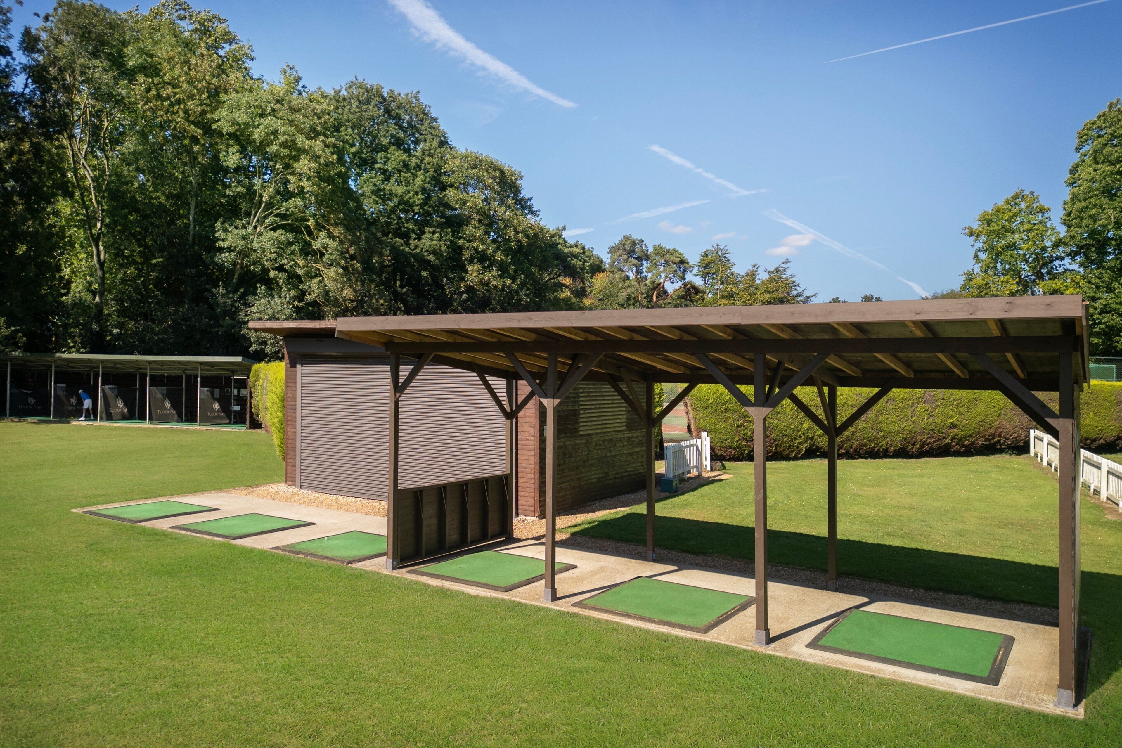 A covered pavilion with a roof and a small adjacent building, surrounded by a well-maintained lawn and trees.