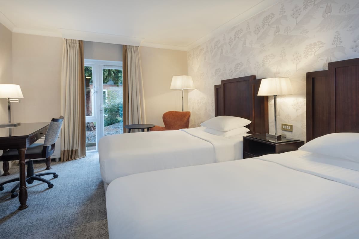 Une chambre d’hôtel avec deux lits, un bureau avec une chaise, une petite table et une chaise.