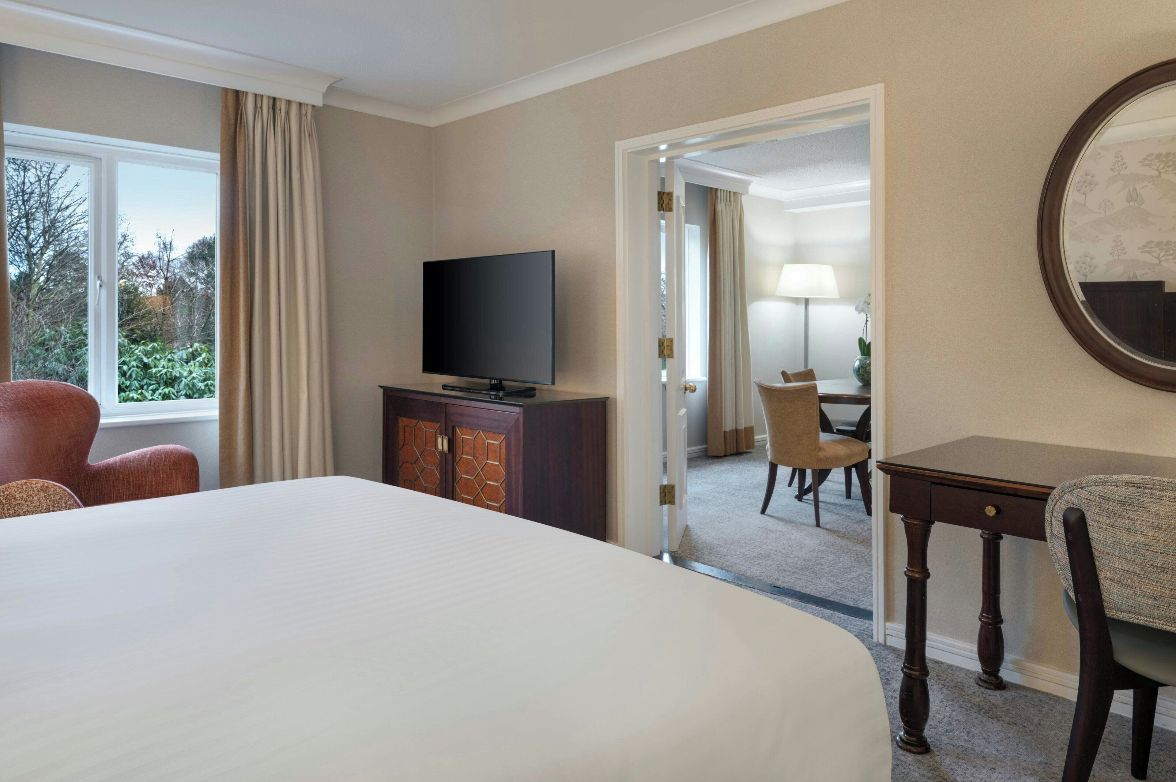Hotelkamer met een groot bed, een televisie op een kast, een bureau met stoel, en uitzicht op het landschap door een raam.