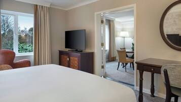 Hotelkamer met een groot bed, een televisie op een kast, een bureau met stoel, en uitzicht op het landschap door een raam.