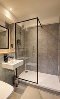 Ein modernes Badezimmer mit einer gläsernen Dusche, einem Waschbecken mit Seifenspender und einer Toilette.