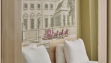 A hotel room with a bed, a bedside table, and a wall-mounted artwork depicting a building and horses.