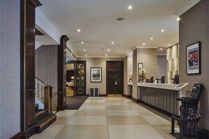 A hotel lobby with a reception desk, a staircase, and a framed picture on the wall.