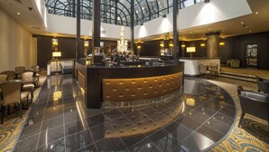 A hotel lobby with a glass ceiling, a reception desk, seating areas, and a patterned carpet. - President Hotel (London)