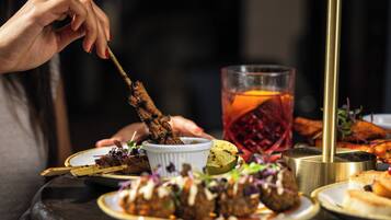 Une table à manger avec différents plats, notamment de la viande grillée sur des brochettes, un verre de boisson et un petit bol de sauce.