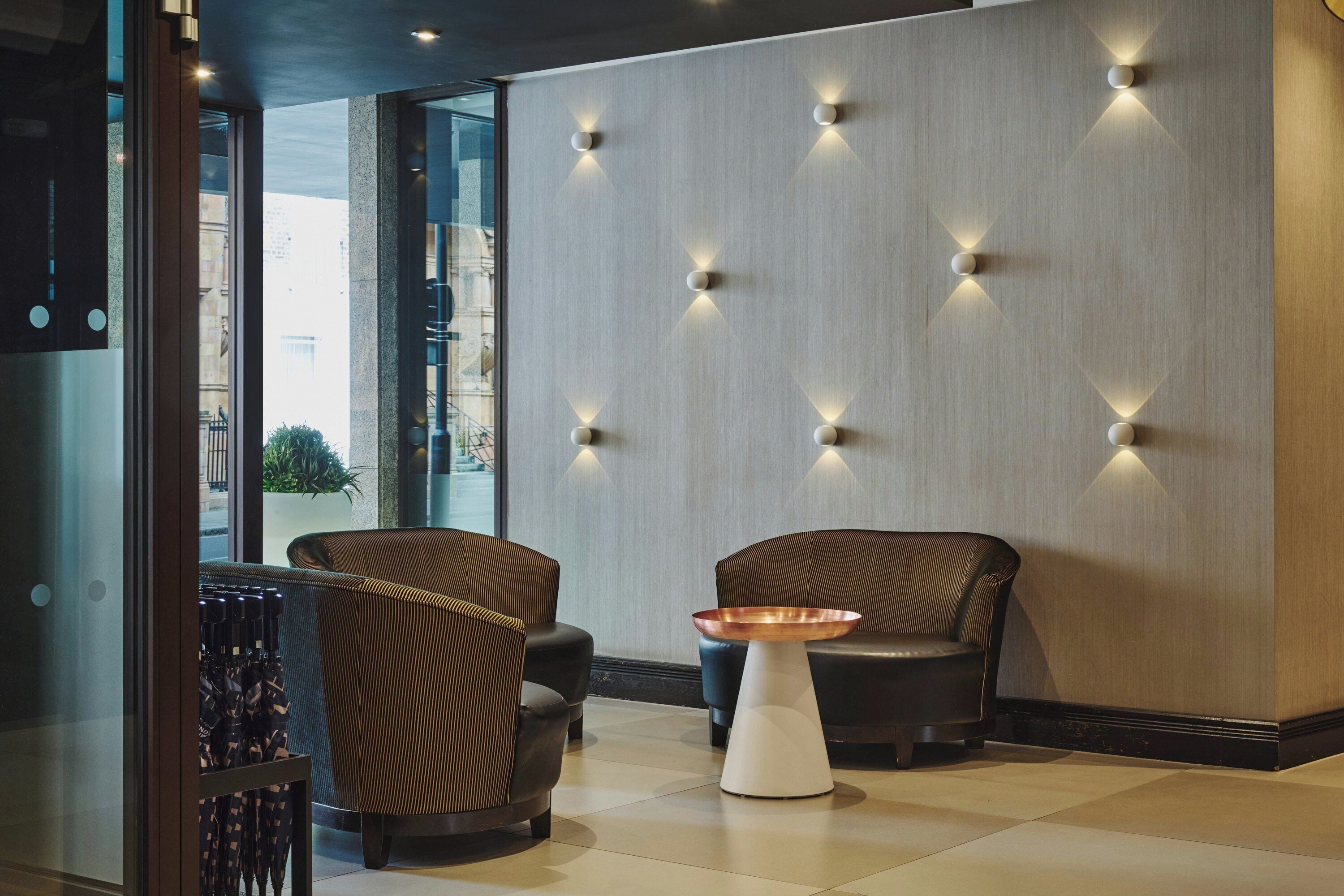 Un interior moderno con dos sofás de cuero, una mesa blanca y una pared con lámparas geométricas.