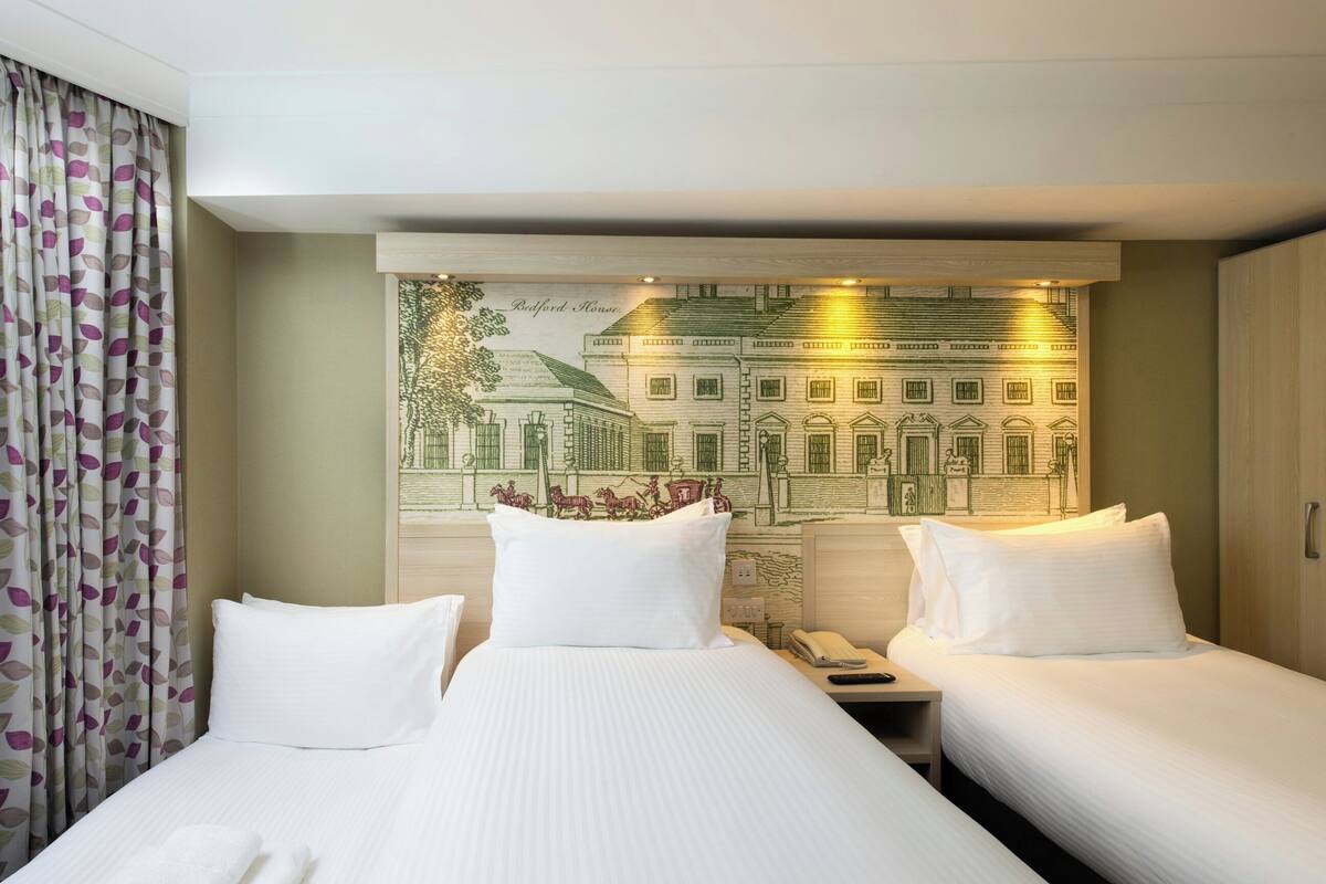 A hotel room with two beds, a large wall mural, and a telephone on the nightstand.