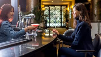 A bar area with a bar counter, a person holding a drink, and another person seated across the counter.