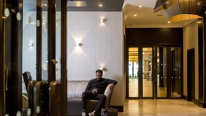 A man sitting on a bench in a hotel lobby with a modern design, including a patterned wall and a large pendant light. - President Hotel (London)
