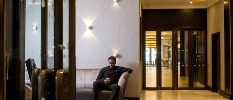 A man sitting on a bench in a hotel lobby with a modern design, including a patterned wall and a large pendant light.