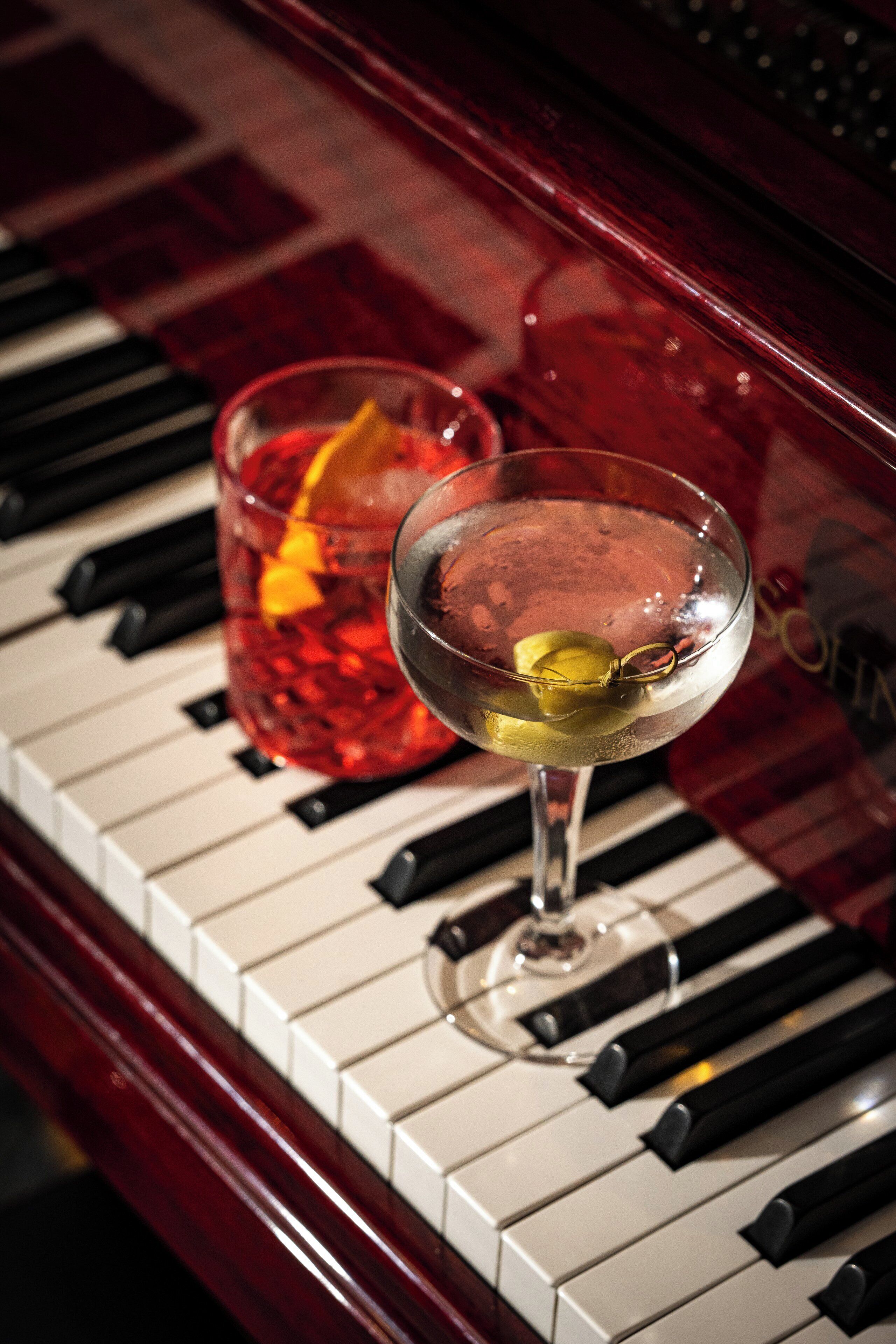 A piano with a glass of wine and a cocktail on top.