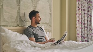 A person sitting on a bed in a hotel room, reading a magazine. - President Hotel (London)