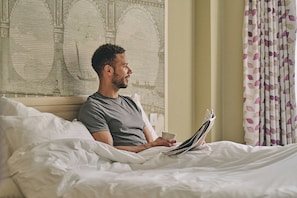 A person sitting on a bed in a hotel room, reading a magazine.