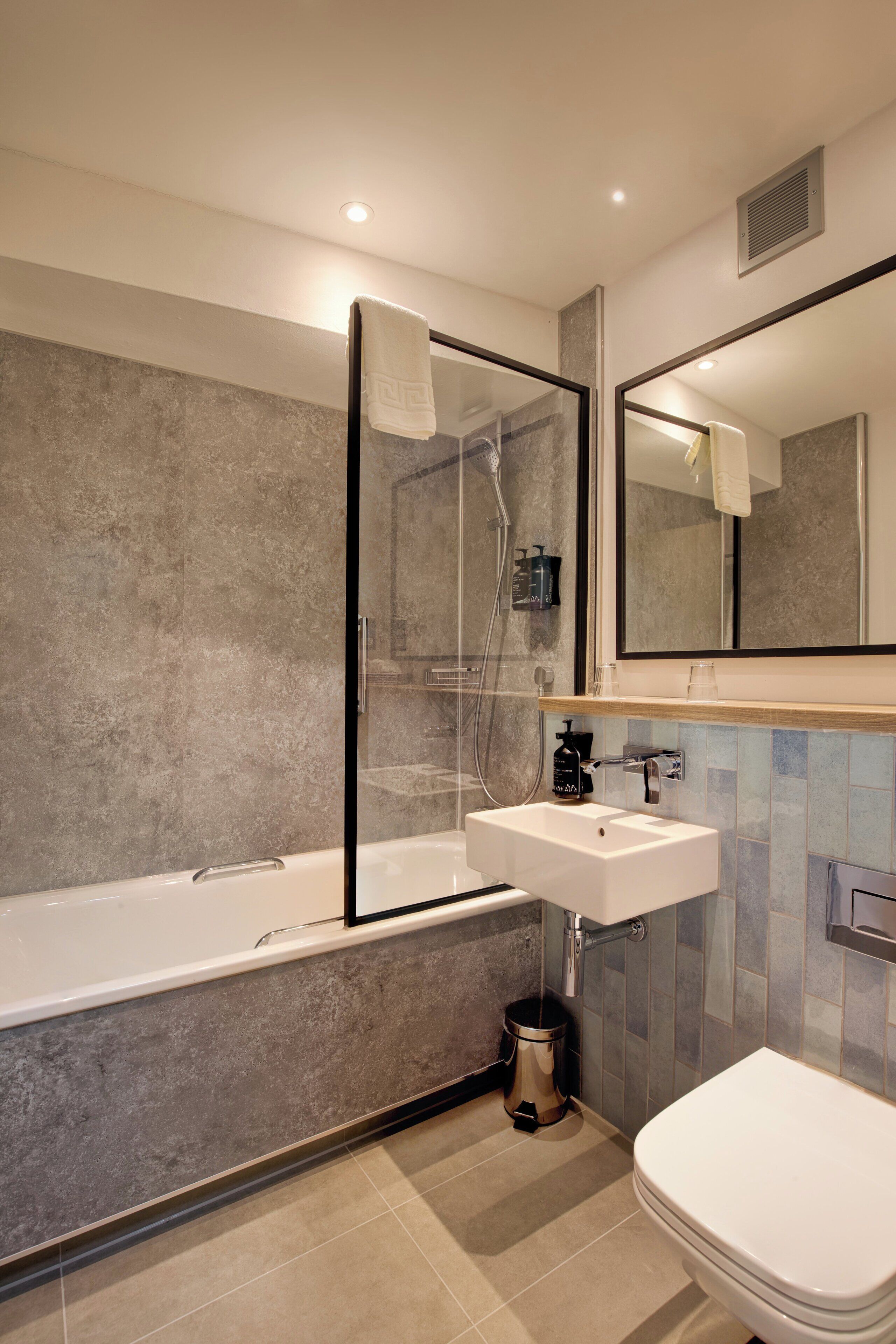 A modern bathroom with a bathtub, a sink, a toilet, and a mirror.