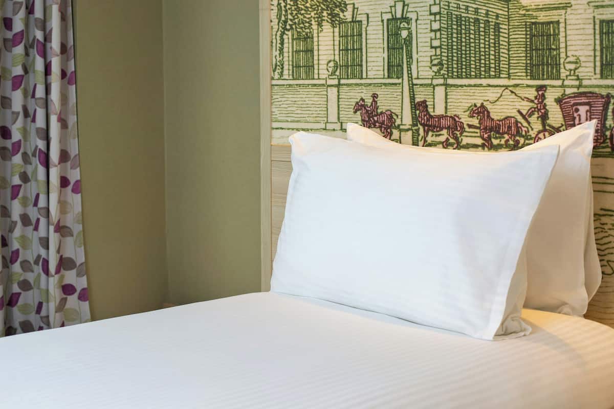 A hotel room with a bed, a curtain with a leaf pattern, and a wall with a green embroidered design.