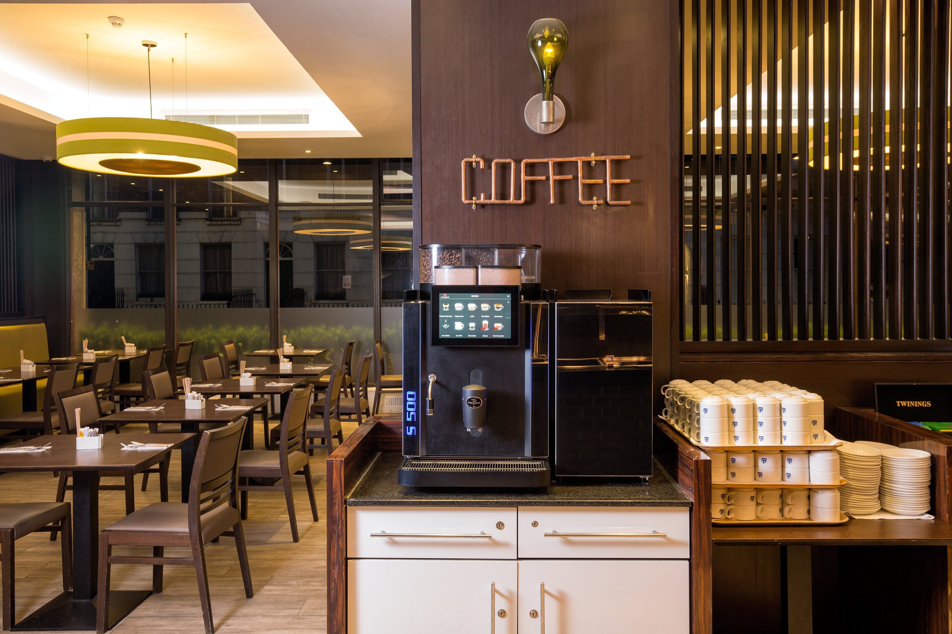 Una estació de cafè moderna amb una màquina de cafè digital, tasses ordenades i un cartell que diu "COFFEE".