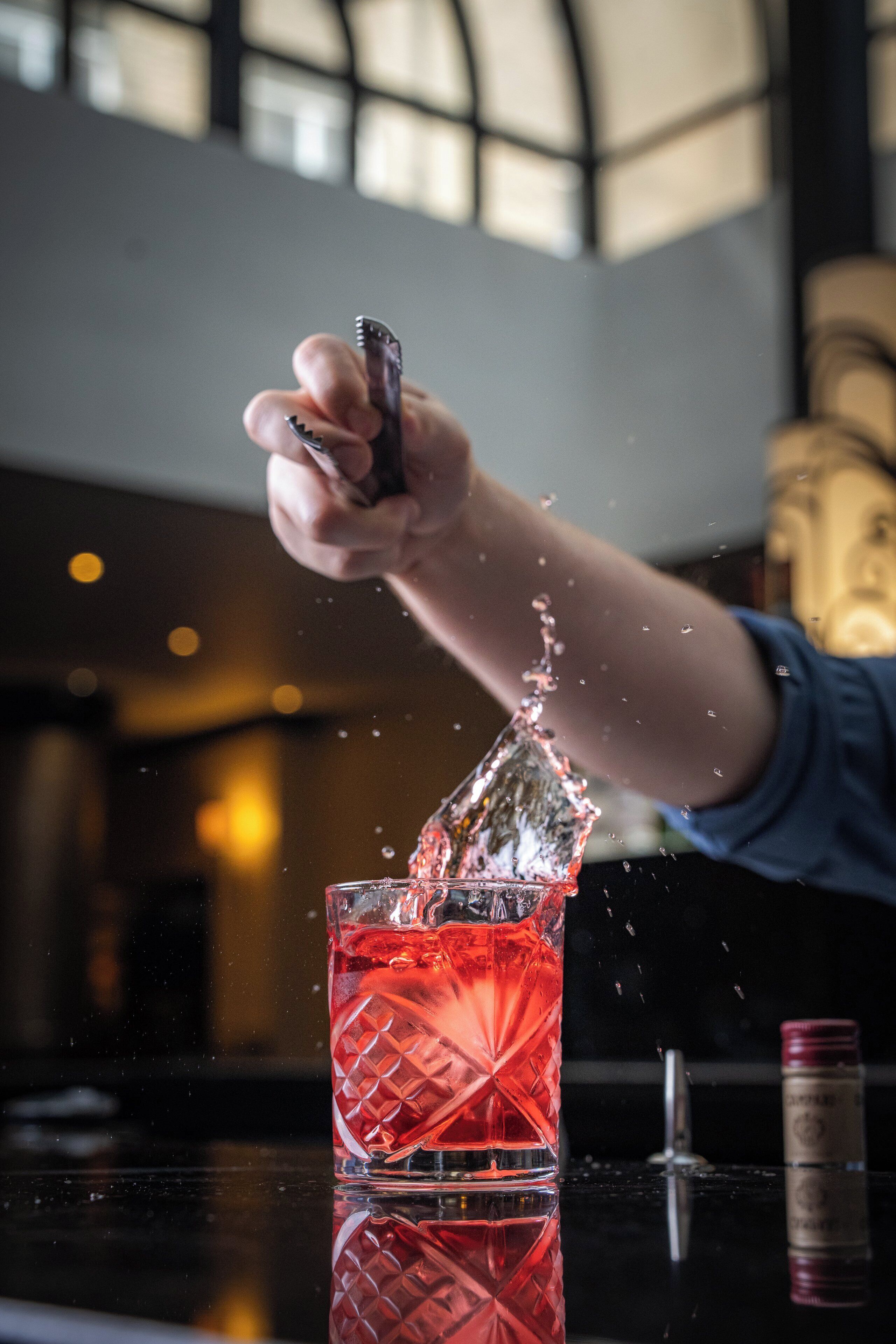 A hand pouring a drink into a glass, with water splashing out.