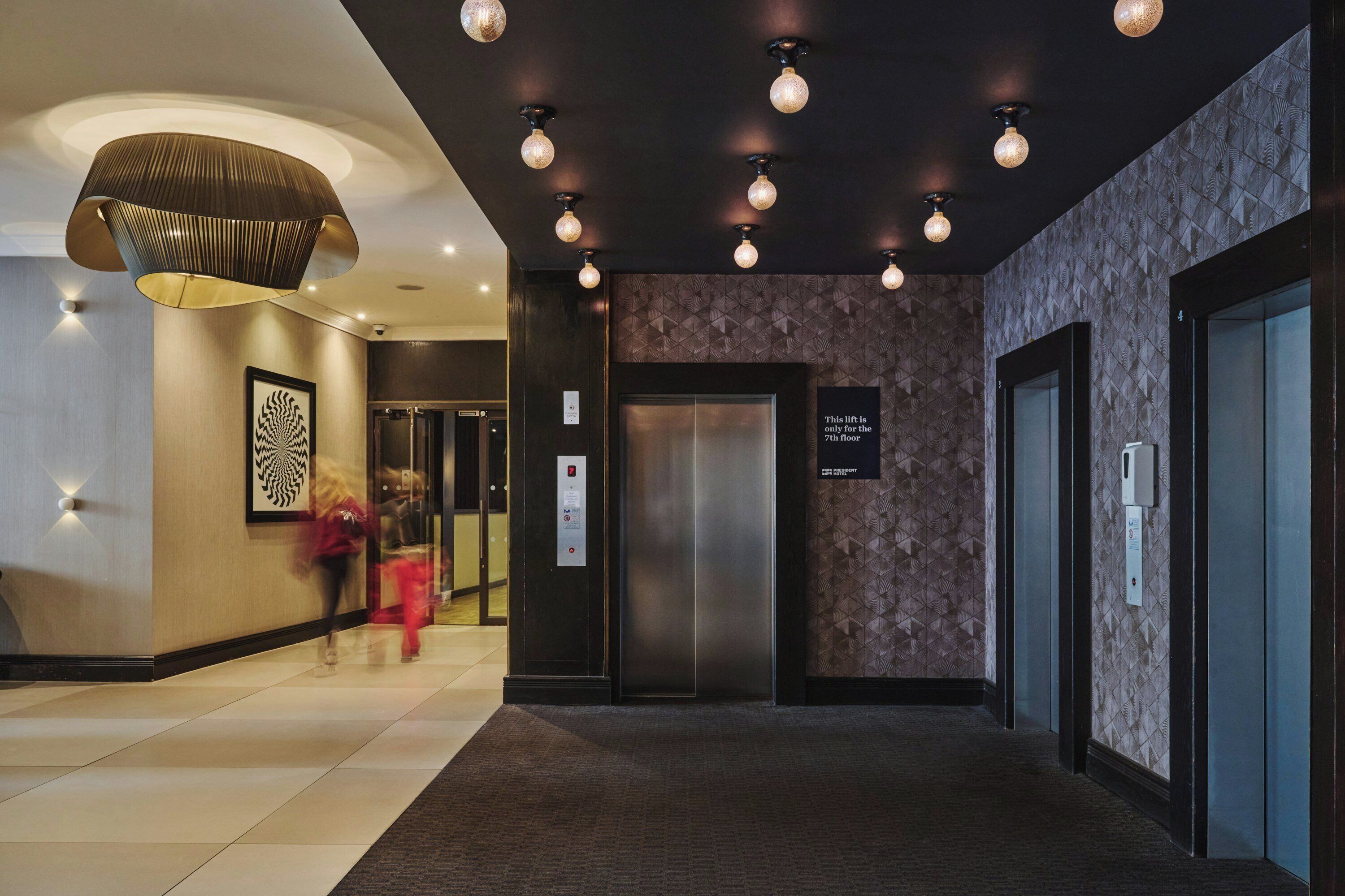 Eine Hotelhalle mit modernem Design, inklusive einer großen Chandelüster, einer Wand mit Musterung und einem Aufzug.