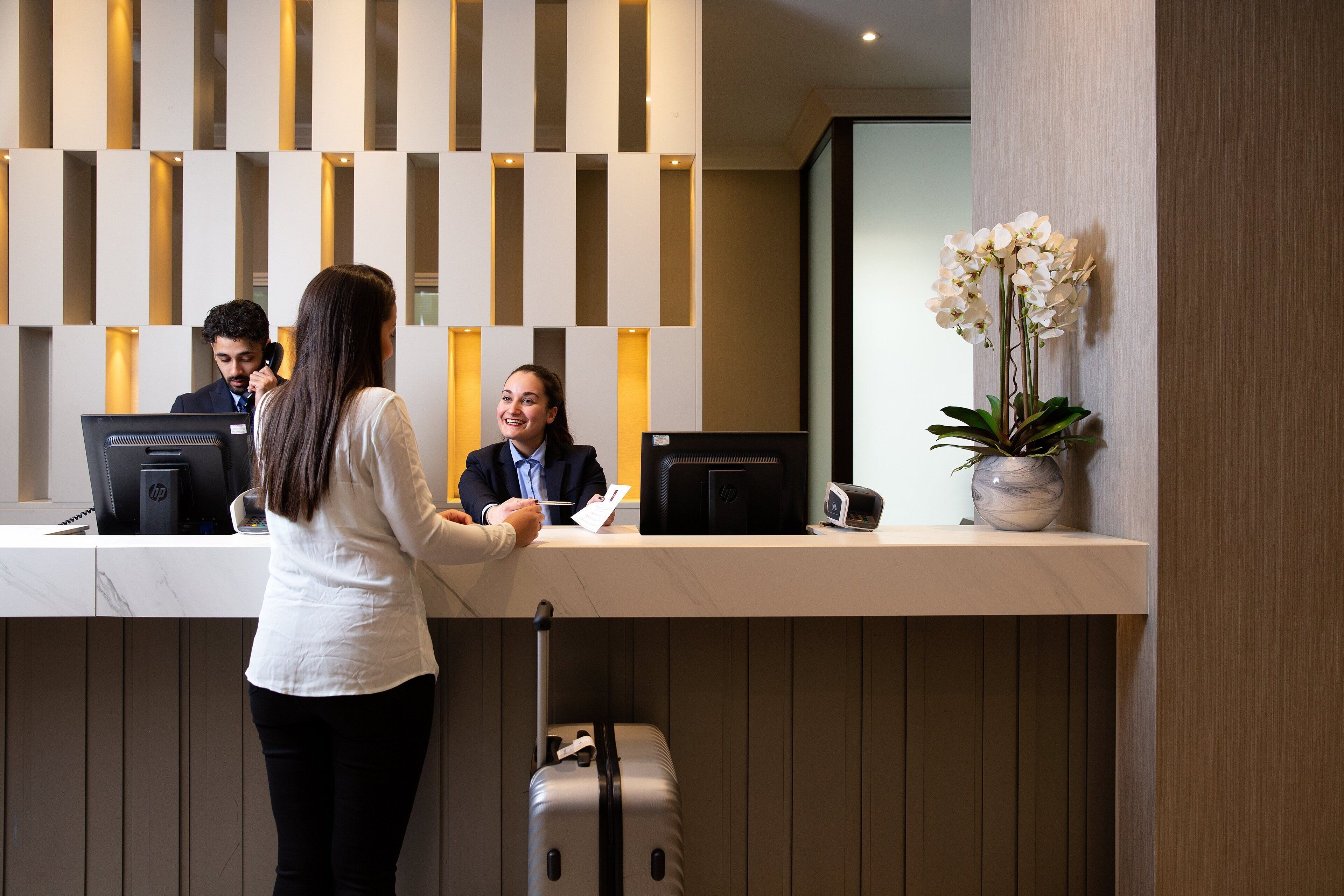 Un mostrador de recepción de diseño moderno, con un panel de luz vertical y un jarrón con flores blancas.