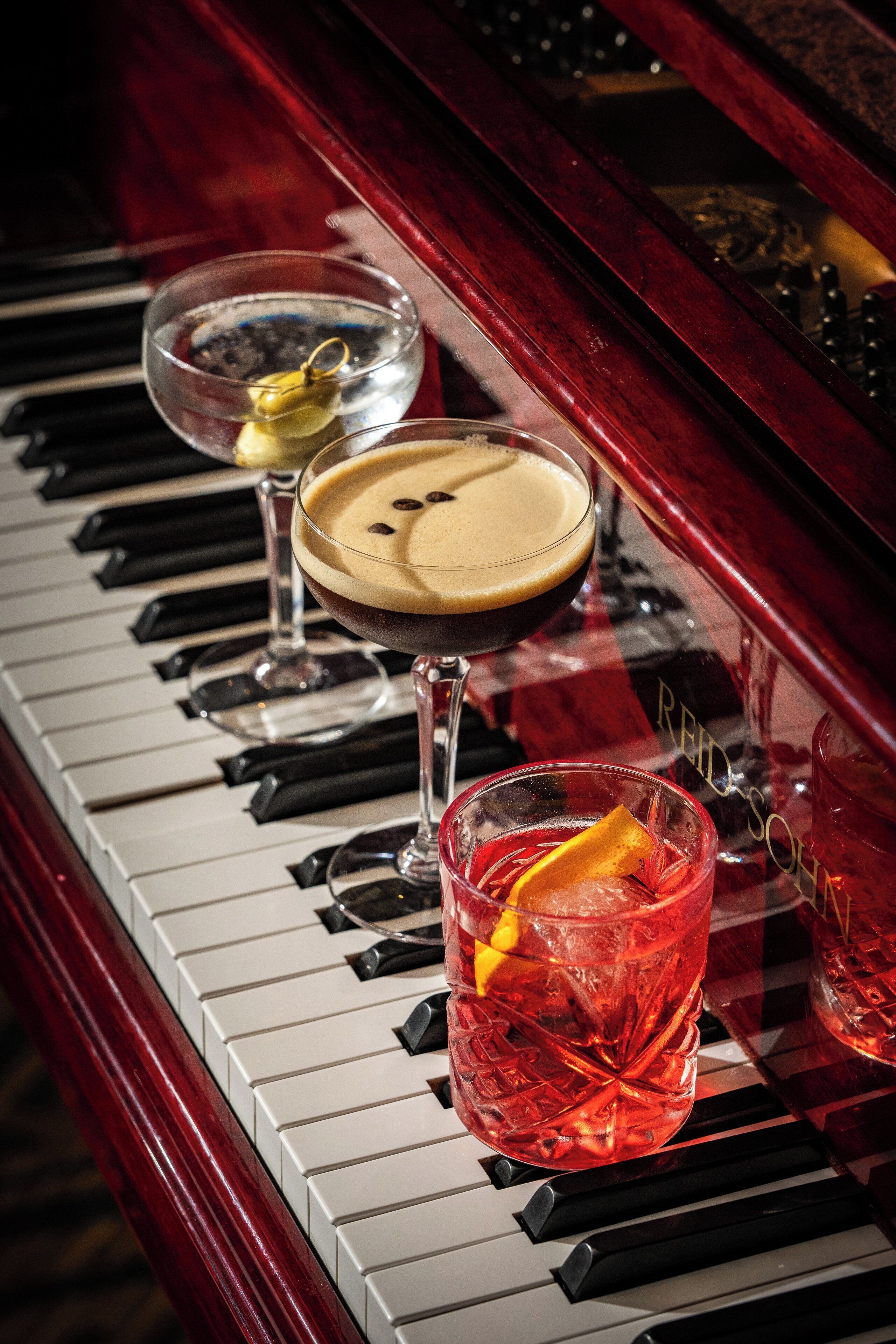 Een piano met drie glazen drank op de toetsen.