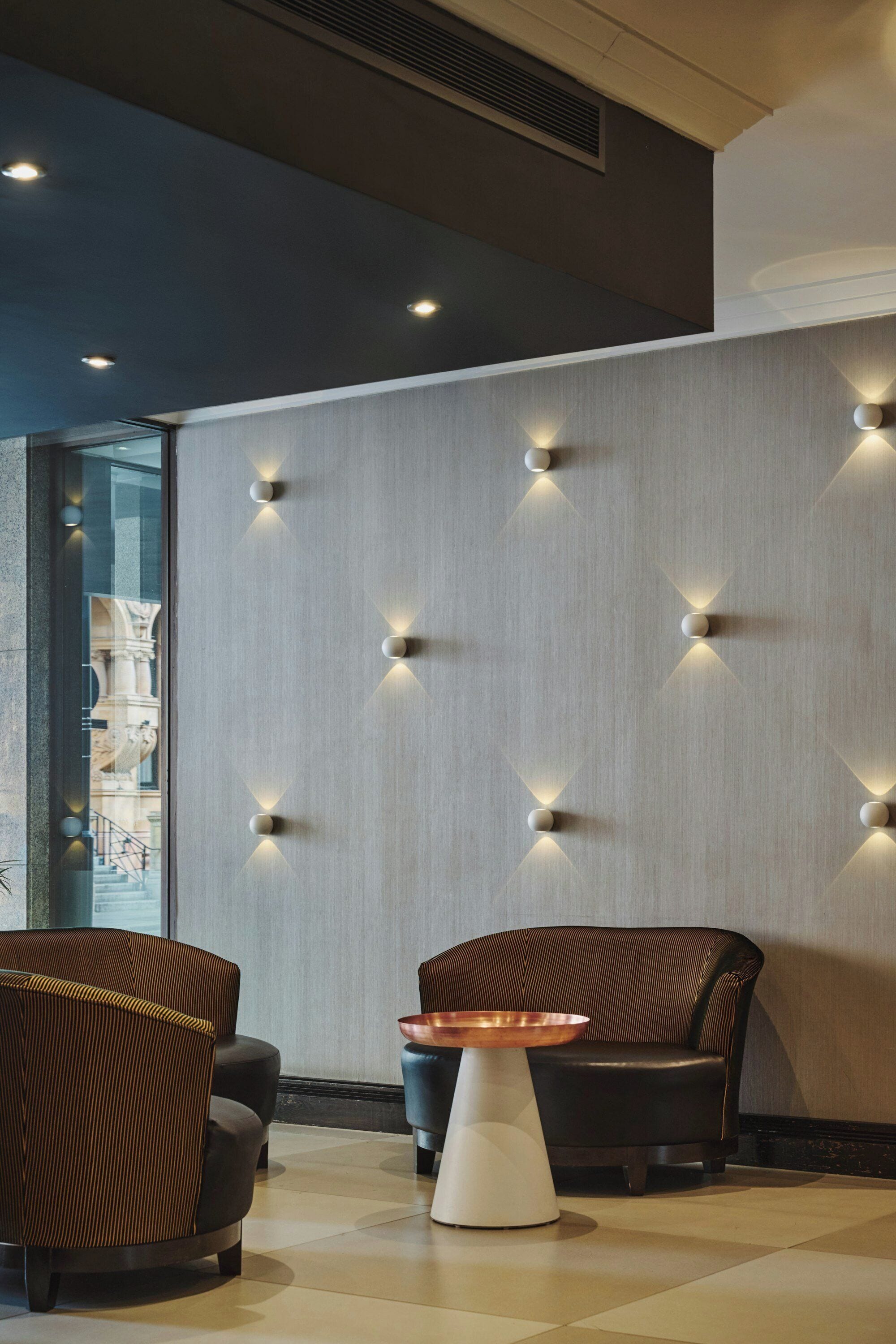 A modern interior with a seating area, a wall with recessed lighting, and a view of an outdoor area.