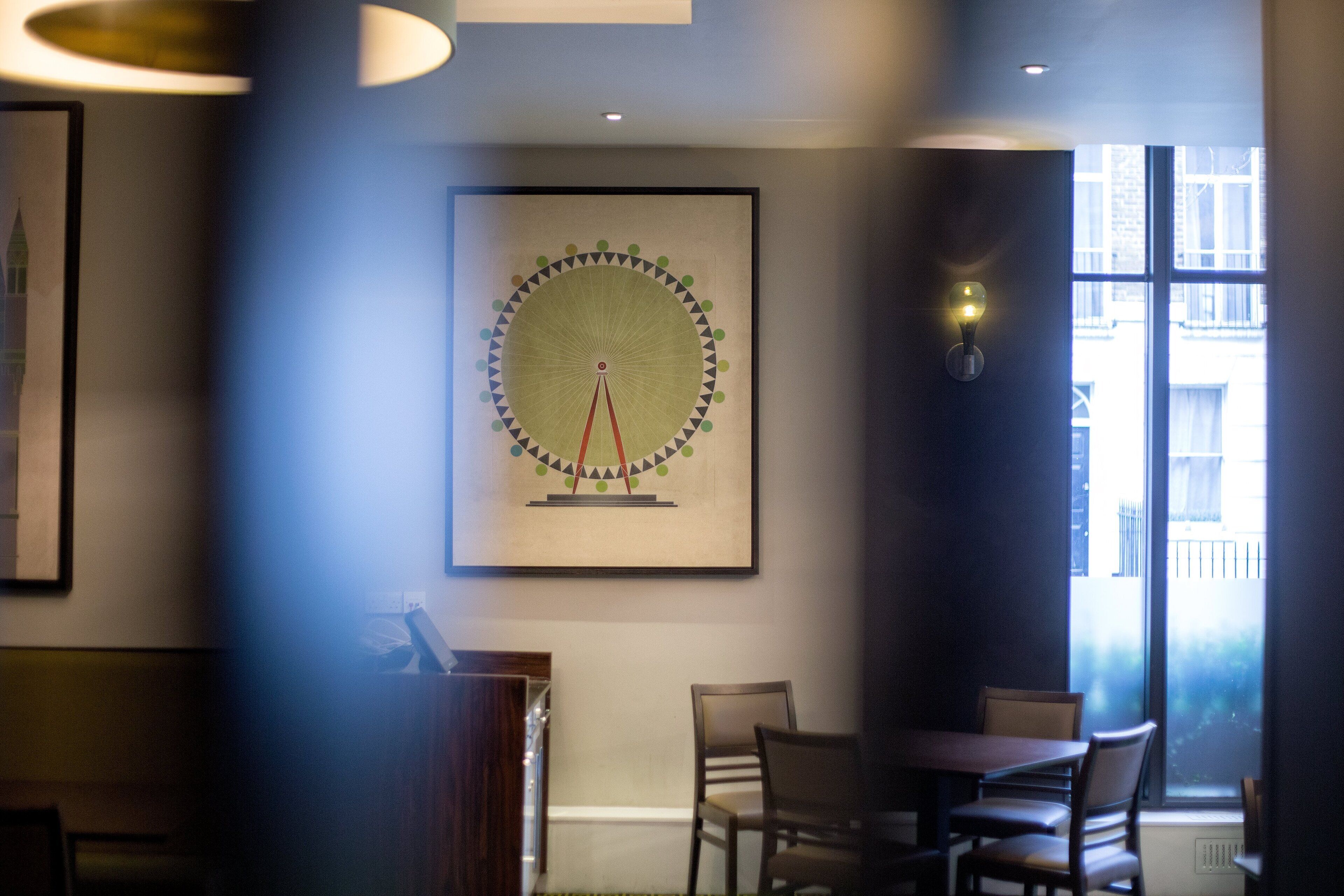 A dining area with a table and chairs, a framed artwork on the wall, and a window with a view of buildings.