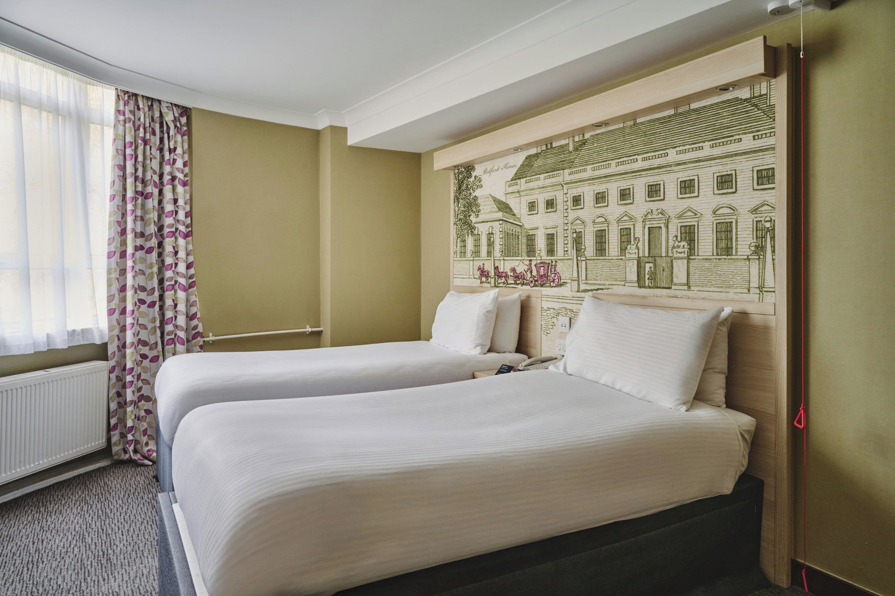 Une chambre d’hôtel avec deux lits, une grande fenêtre avec des rideaux légers et une fresque murale.