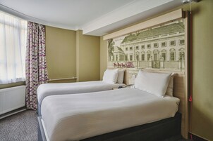 A hotel room with two beds, a large window with sheer curtains, and a wall mural.