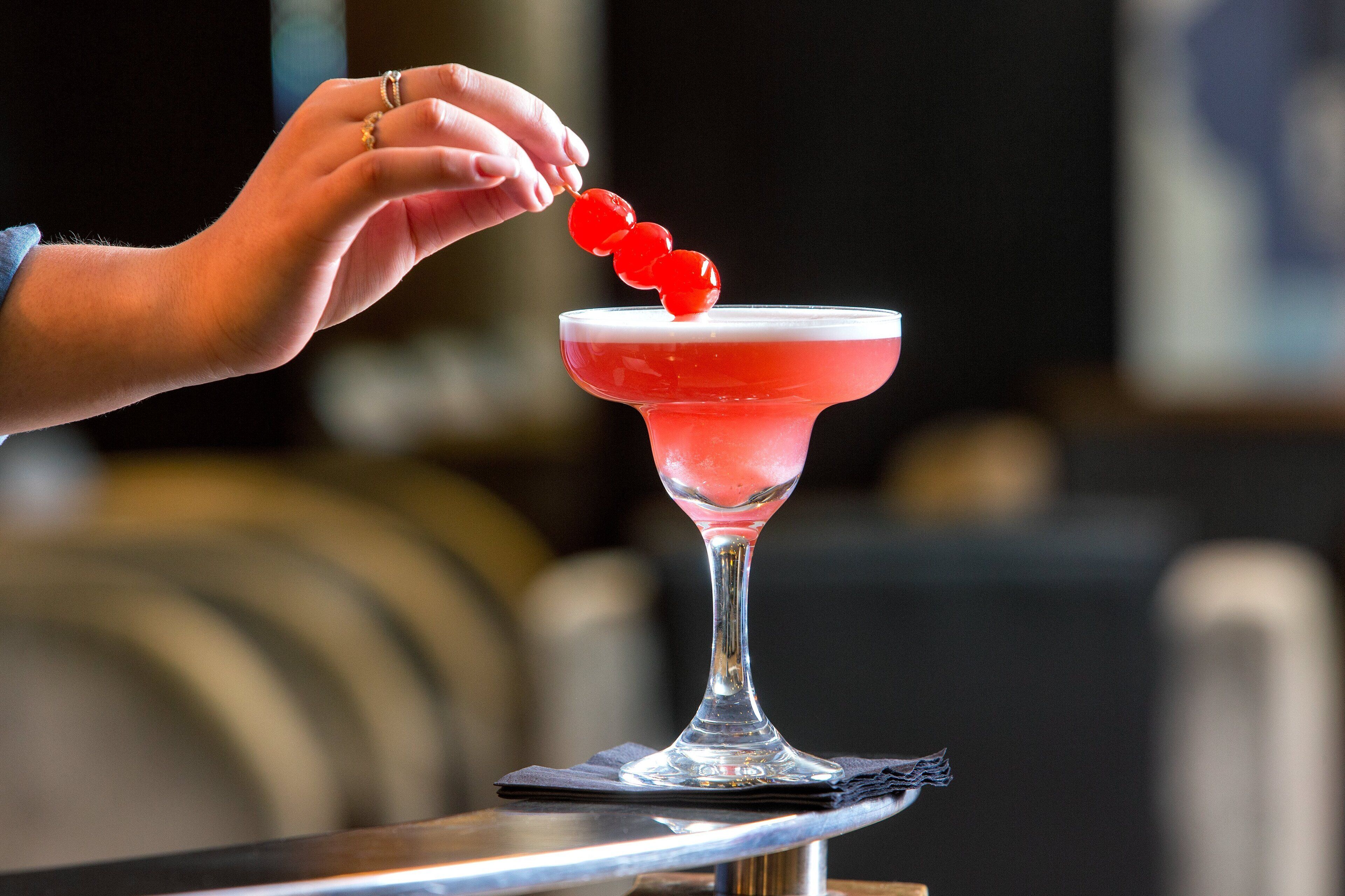 Une main tenant une décoration de cocktail au-dessus d’un verre à martini rempli d’une boisson rouge.