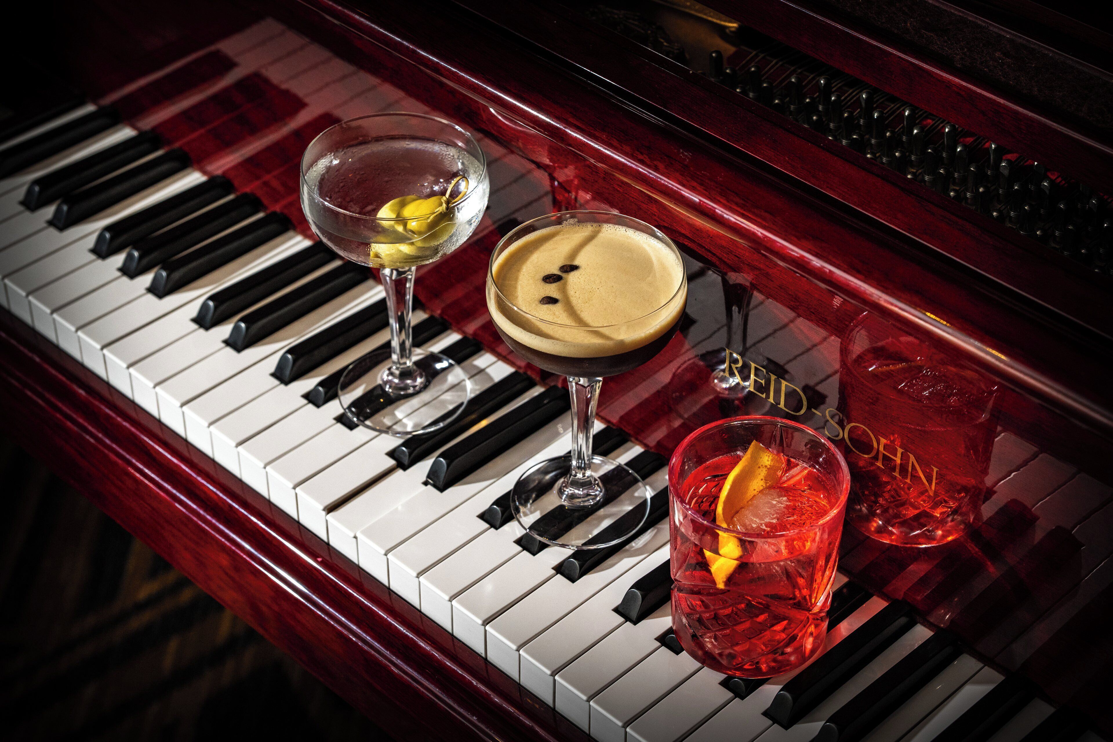 A grand piano with three glasses of beverages on its keys.