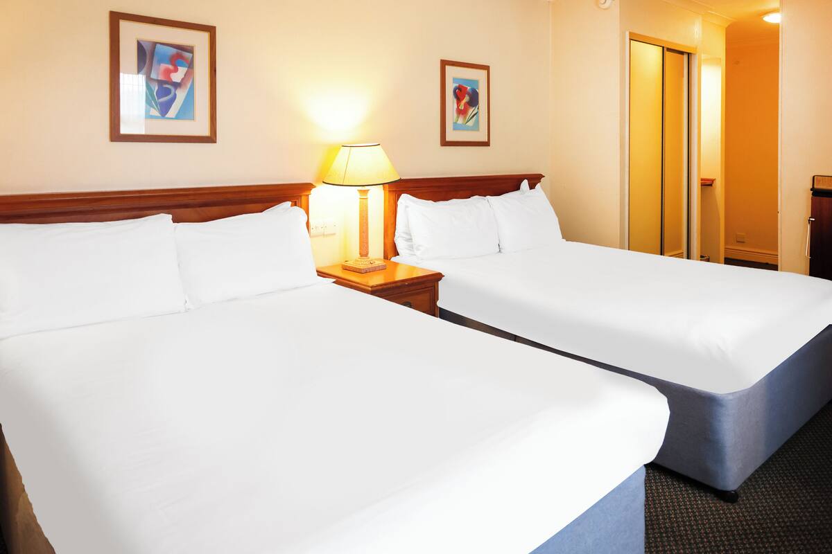Una habitación de hotel con dos camas individuales, una mesita de noche con lámpara y dos cuadros enmarcados en la pared.