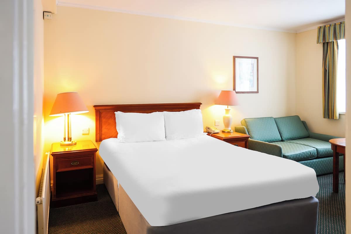 Una habitación de hotel con una cama grande, dos mesitas de noche con lámparas, un sofá verde y una pequeña mesa.