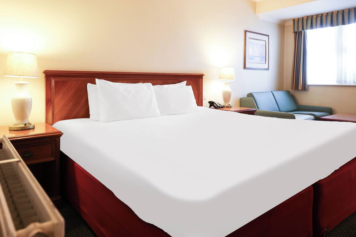 Habitación de hotel con una cama grande, dos mesitas de noche con lámparas, un escritorio y una silla.