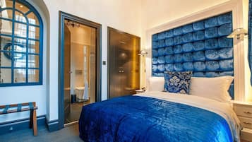 Une chambre à coucher avec un grand lit, une tête de lit bleue, un banc et une salle de bain visible à travers une porte ouverte.