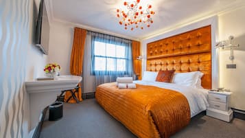 A hotel room with a large bed, a bedside table, a nightstand, a wall-mounted TV, and a window with curtains.