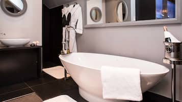 Une salle de bain moderne avec une baignoire sur pieds, un miroir rond, un lavabo et une bouteille de champagne.