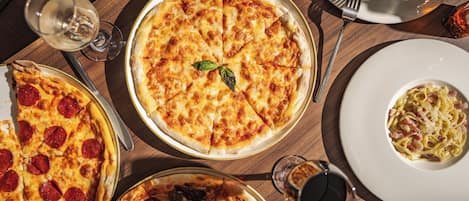 A dining table with multiple pizzas and a plate of pasta.