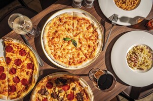 A dining table with multiple pizzas and a plate of pasta.