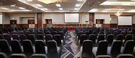 A conference room with rows of chairs, a large screen, and a chandelier.