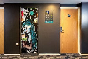 A hotel corridor with a wall mural, a sign indicating room numbers, and a door labeled 'City Sleeper'.